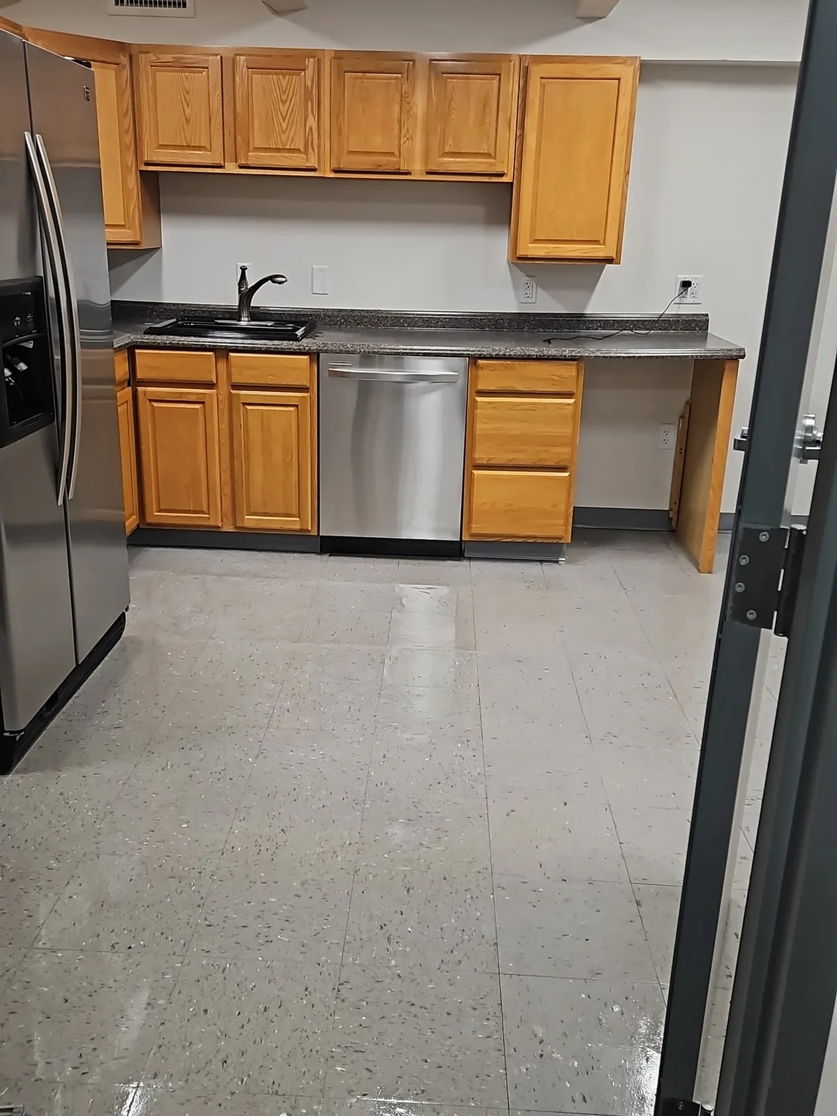 Commercial kitchen with wood cabinets, stainless steel appliances, and a reflective tile floor